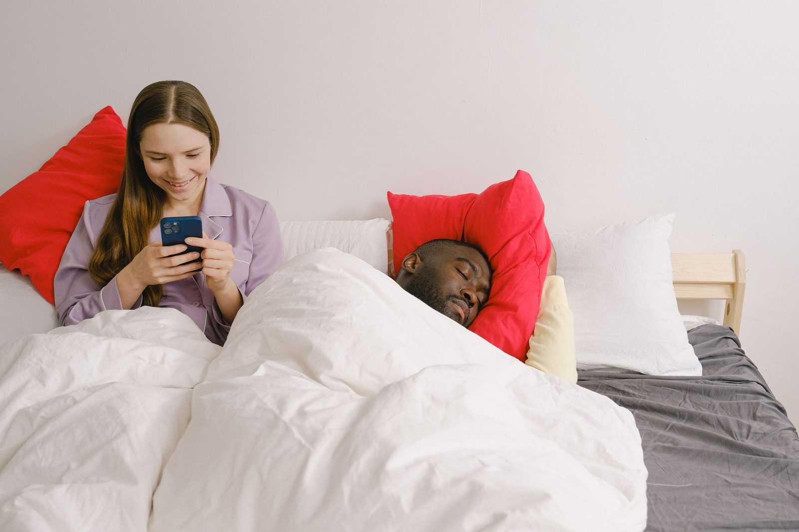 Uma mulher sorridente em seu telefone ao lado de um homem dormindo em um aconchegante quarto