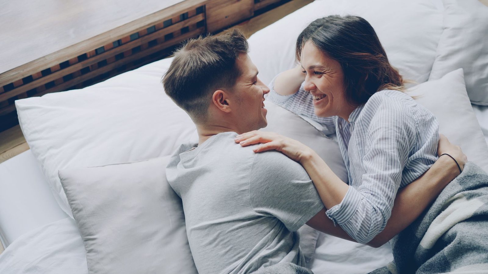 Um momento de alegria em que um casal ri e se abraça na cama, transmitindo amor e felicidade