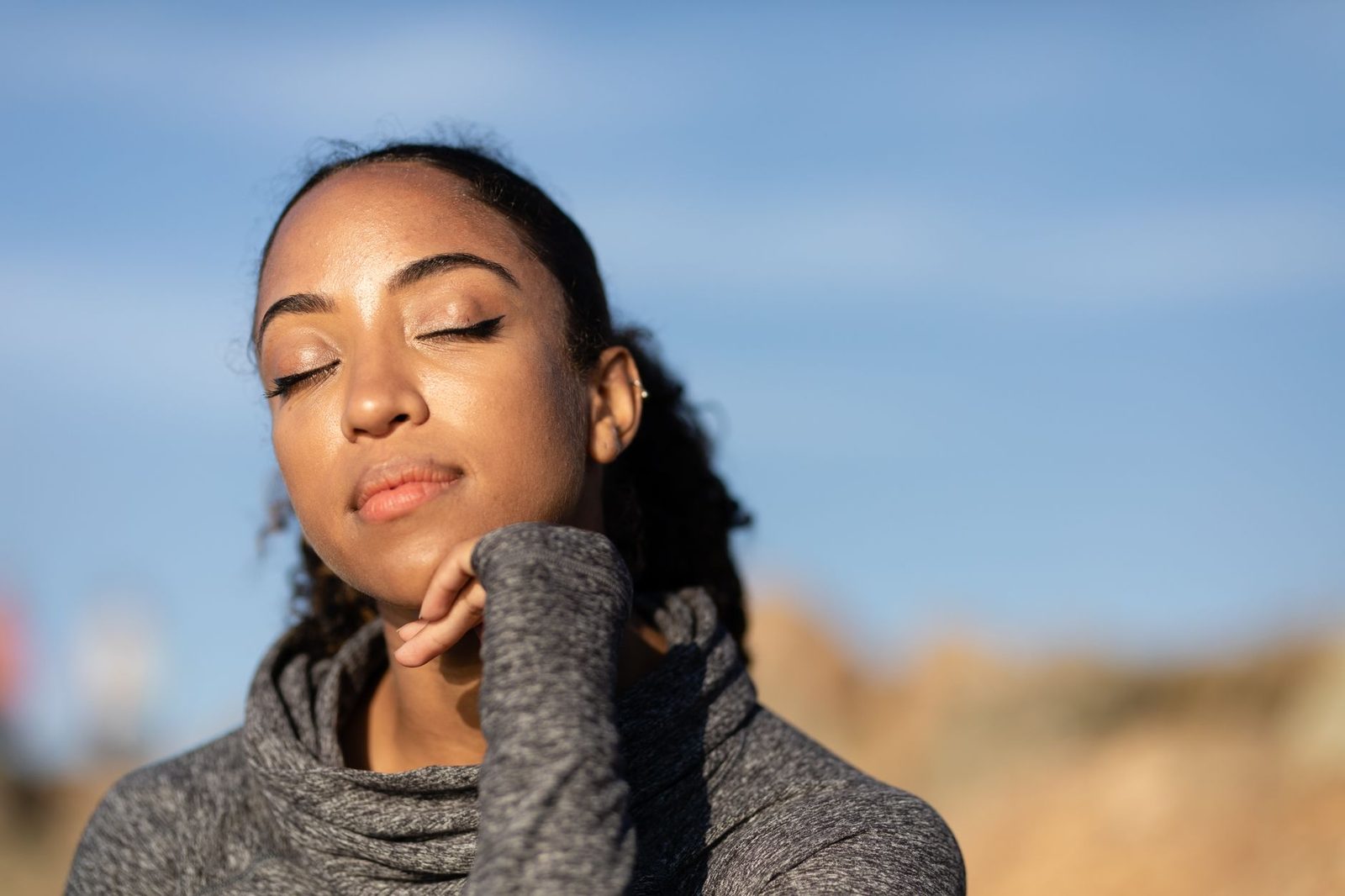 Uma mulher serena com os olhos fechados, desfrutando da luz do sol ao ar livre. Fundo desfocado suave