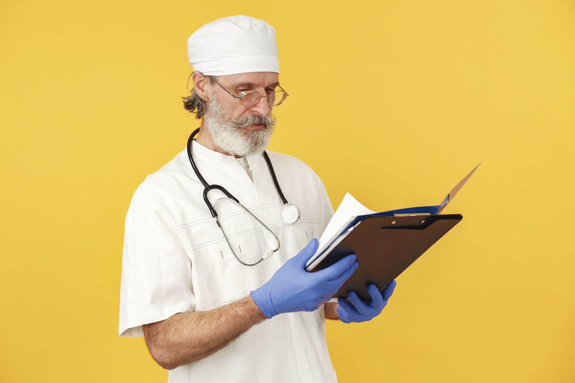 Um médico masculino com barba e estetoscópio revisa documentos médicos sobre um fundo amarelo