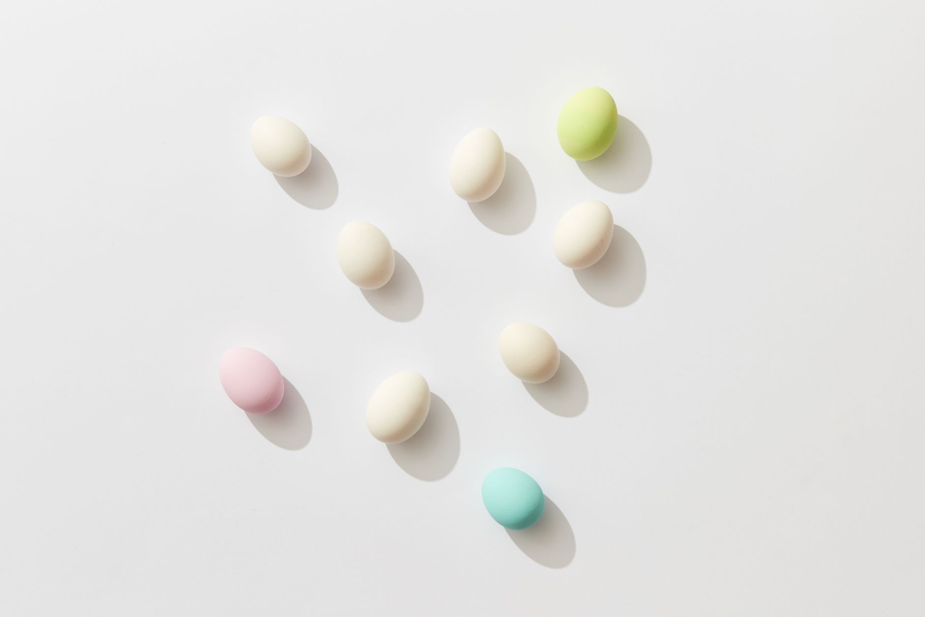 Ovos em tons pastel espalhados sobre fundo branco, vistos de cima